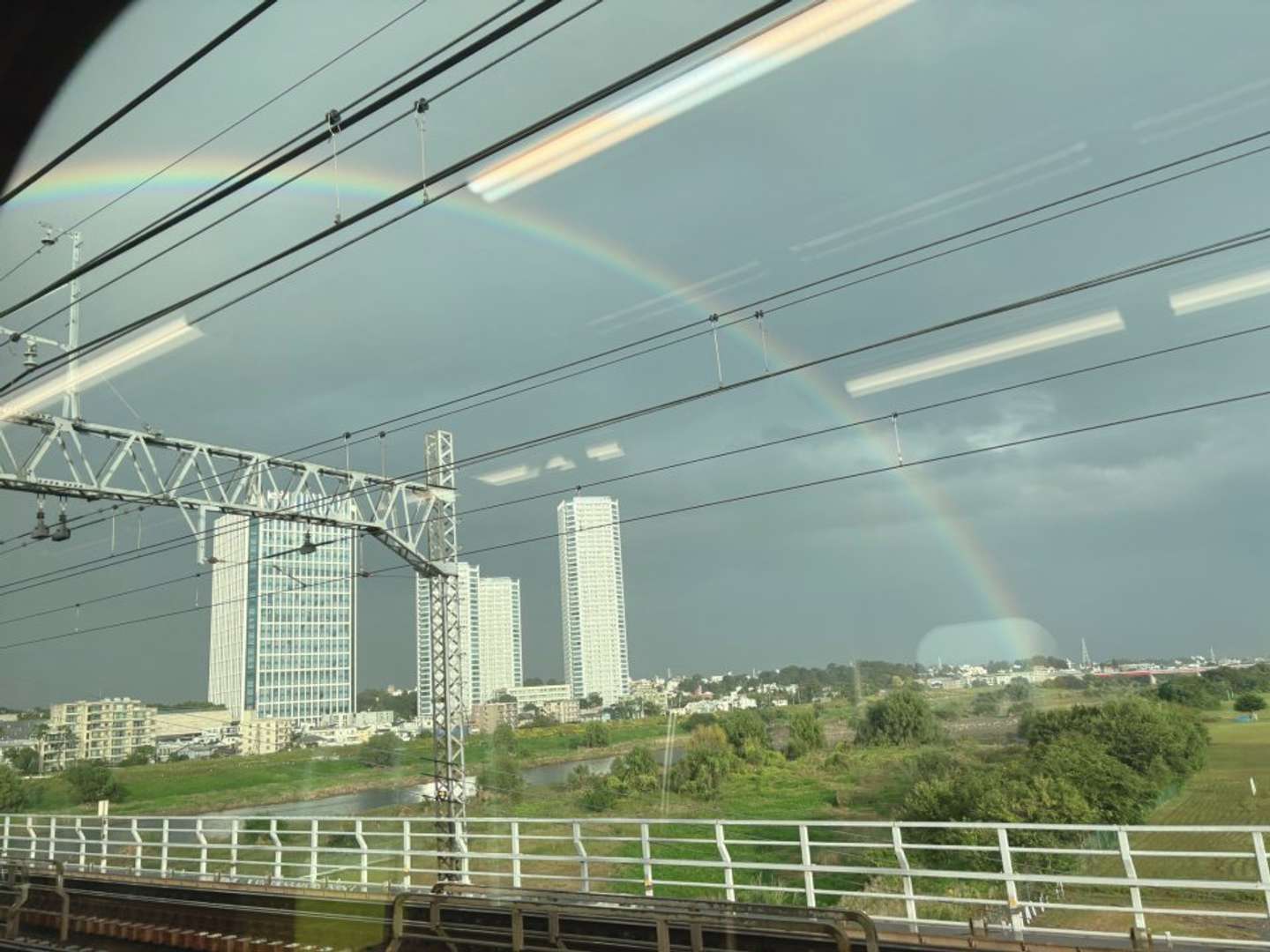 高層ビルが立ち並ぶ街と緑の広がる景色の上に、さらに大きな弧がくっきりと浮かんでいる（画像はぷぎさんの投稿より）